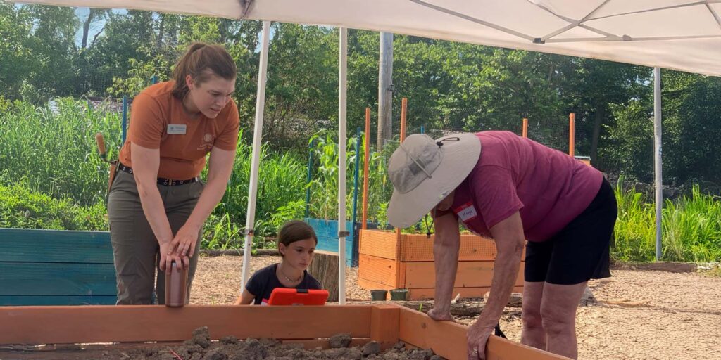 Adult and child participate in outdoor archaeology activity with ARI educator under a canopy