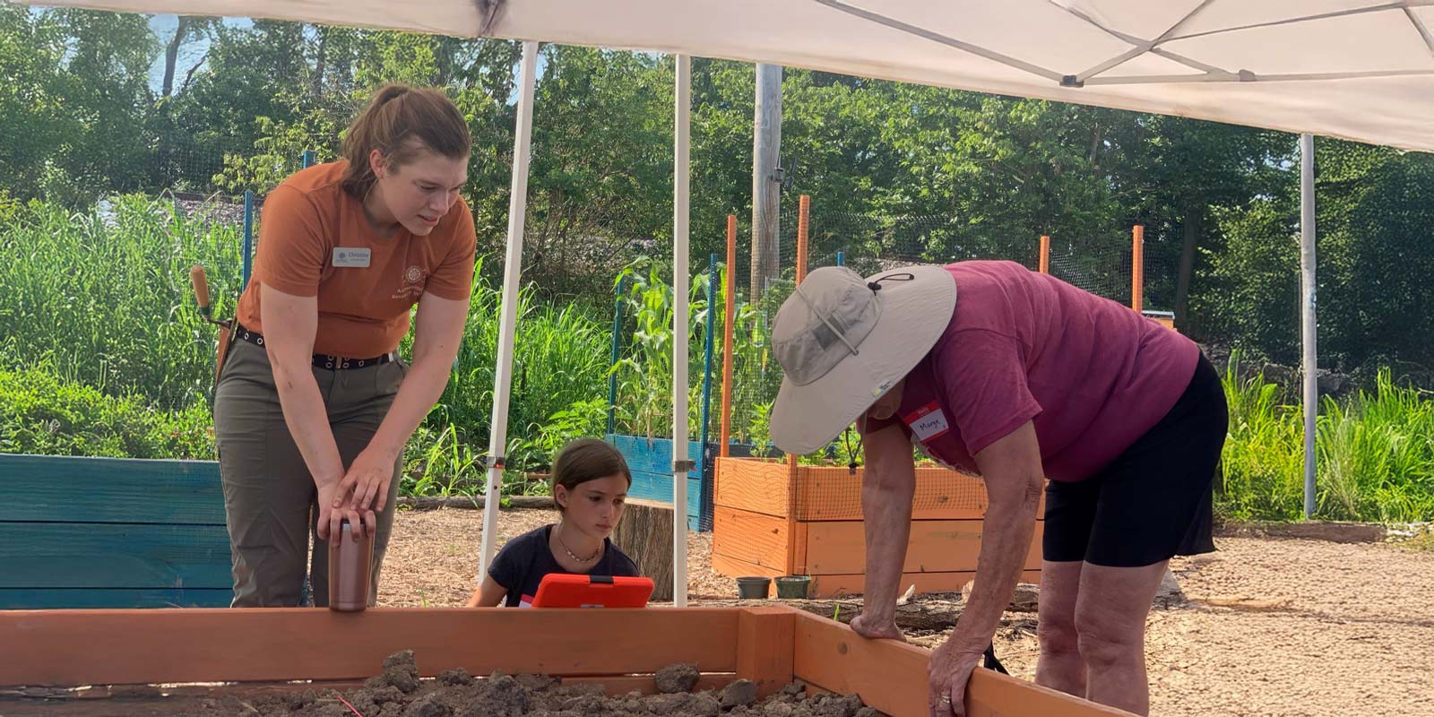 Adult and child participate in outdoor archaeology activity with ARI educator under a canopy