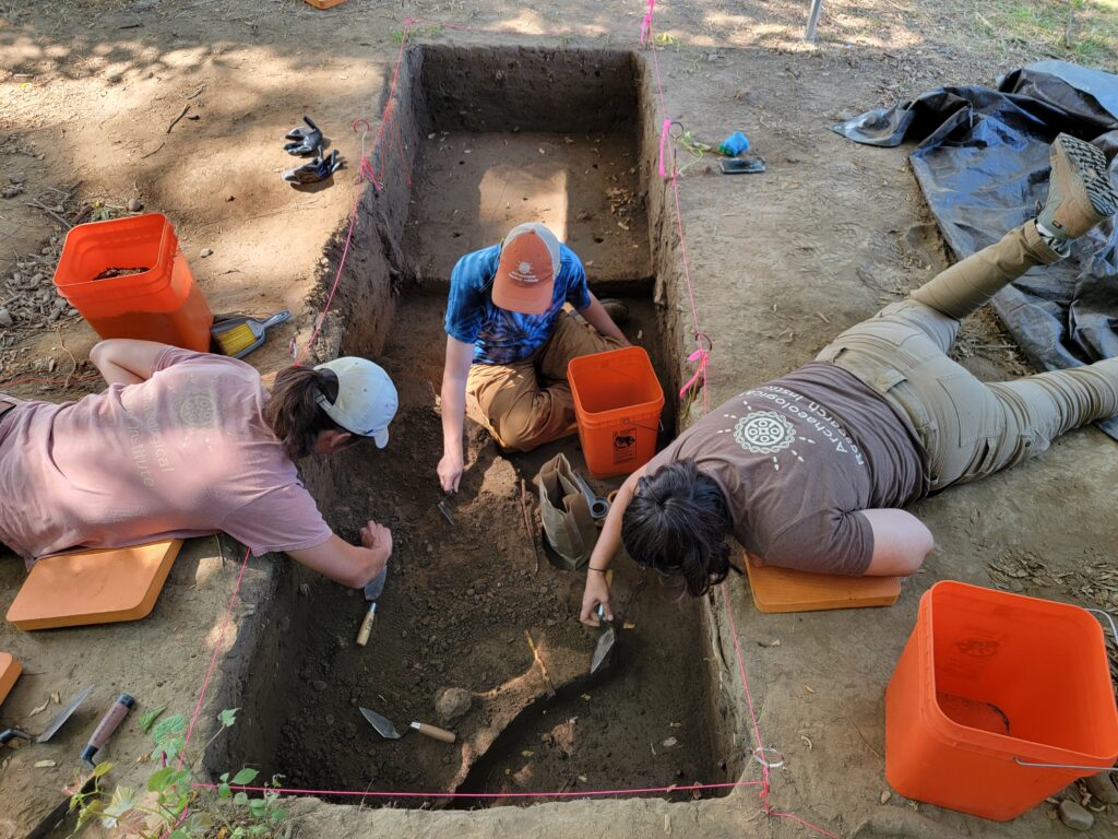 ARI archaeologists carefully excavate an archaeological site, using hand tools to uncover and document layers of soil within a marked excavation trench