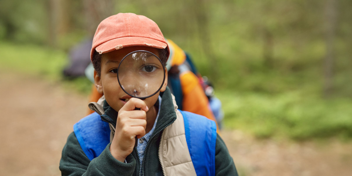 Student participating in an ARI archaeology field exploration outdoors with a magnifying glass