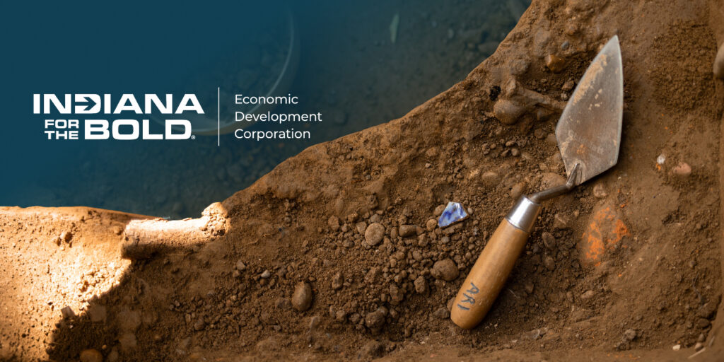 Archaeological dig featuring a trowel and partially uncovered blue artifact, representing historic preservation and Indiana Economic Development Corporation grant opportunities