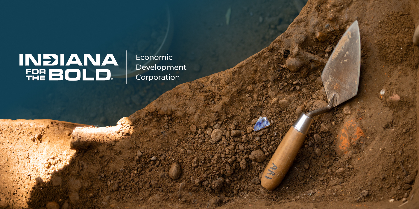 Archaeological dig featuring a trowel and partially uncovered blue artifact, representing historic preservation and Indiana Economic Development Corporation grant opportunities