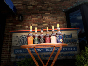 A collection of Weller bourbon bottles displayed outdoors on a round table in front of a bourbon education and research center.
