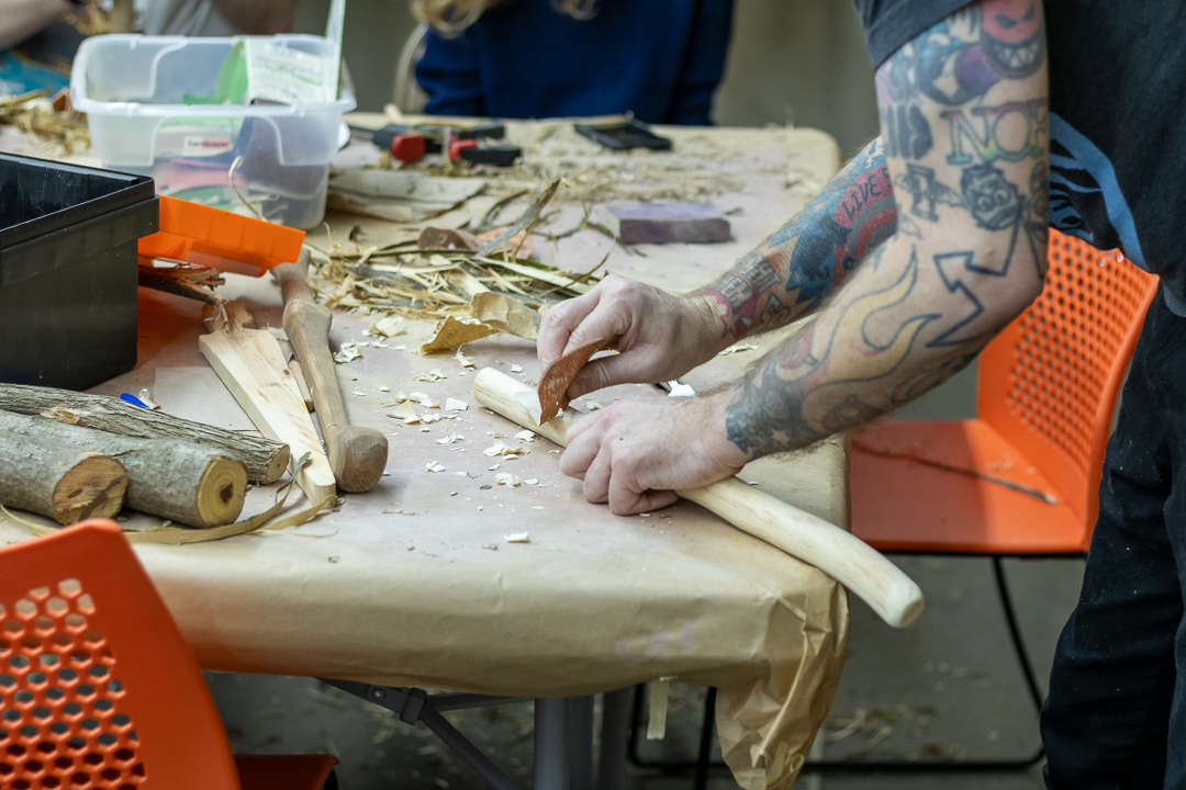 Close-up of participant carving wood with traditional tools during a hands-on experimental archaeology workshop.
